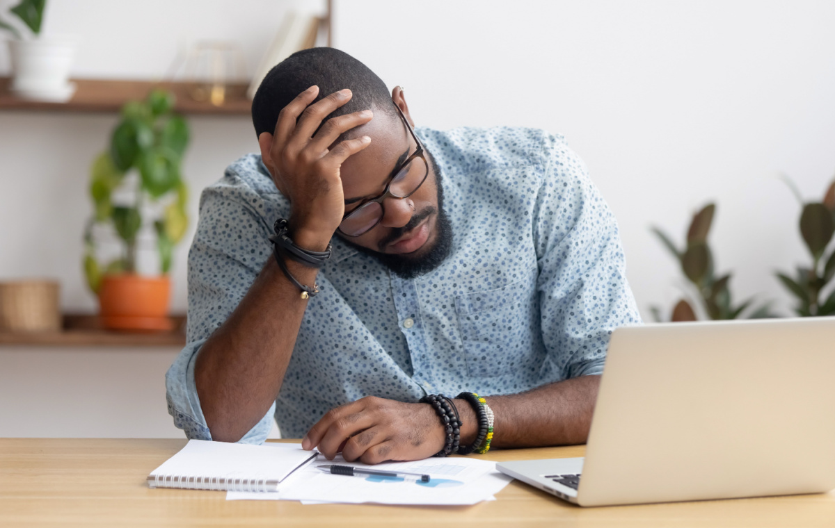 Frustrated African American business man with his head in his hand staring at his laptop