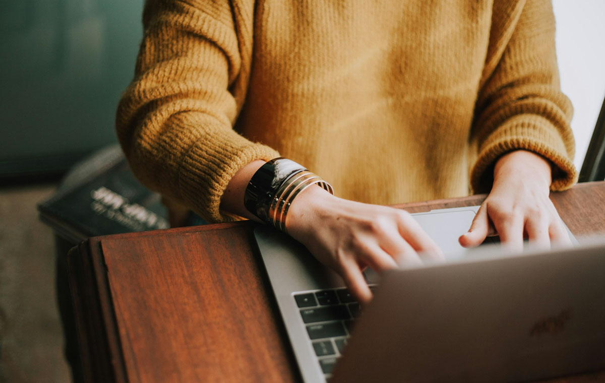 woman wearing a yellow sweater wroking on content marketing for a B2B on a laptop.